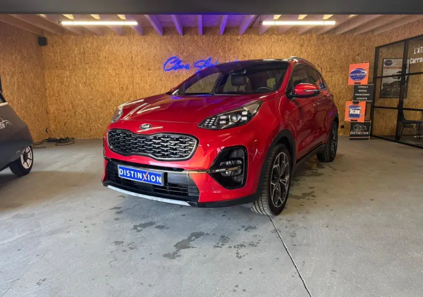 KIA Sportage 1.6 CRDI rouge en 3/4 avant droit, avec calandre noire et jantes alliage visibles en intérieur showroom.
