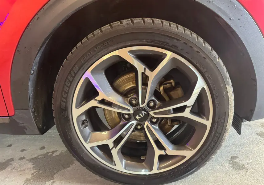 Gros plan sur la roue avant droite d’un KIA Sportage rouge, avec jante alliage et pneu Michelin Pilot Sport.