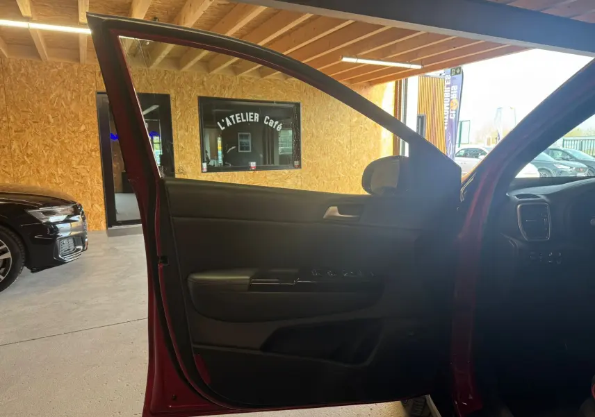 Porte avant gauche ouverte d’un KIA Sportage rouge 2019, mettant en valeur l’intérieur noir et les commandes de la portière.