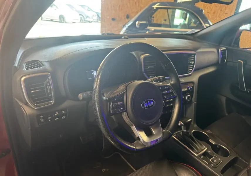 Vue intérieure du poste de conduite du Kia Sportage rouge 2019, avec volant cuir noir et tableau de bord moderne.