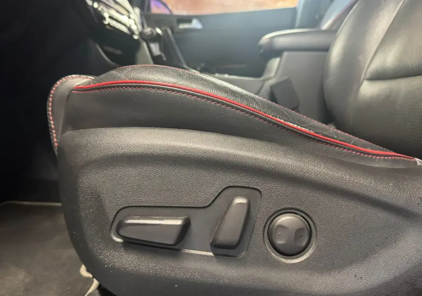Gros plan sur les commandes électriques du siège avant en cuir noir avec surpiqûres rouges du Kia Sportage 2019.