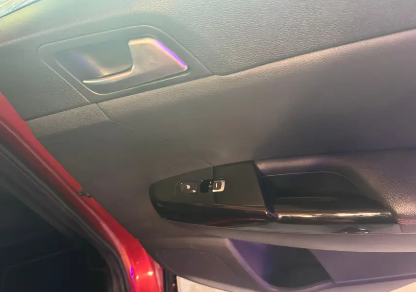 Vue rapprochée de la porte avant gauche rouge du Kia Sportage 2019 avec commandes de vitres et poignée intérieure noire.