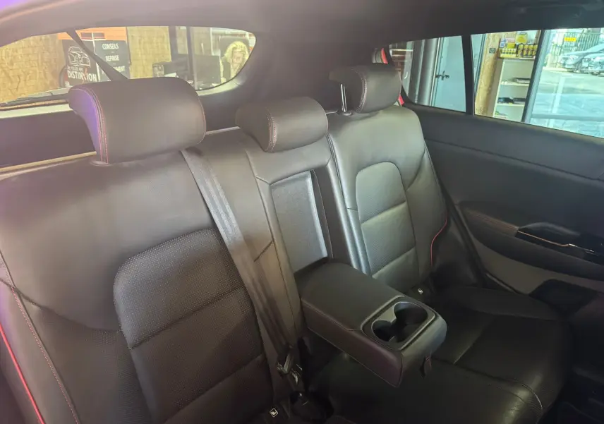 Vue intérieure du siège arrière droit en cuir noir avec accoudoir central et porte-gobelets du Kia Sportage rouge 2019.