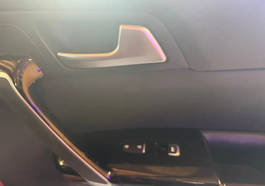 Détail de la porte intérieure côté gauche d’un KIA Sportage rouge 2019, avec poignée argentée et commandes de vitres.