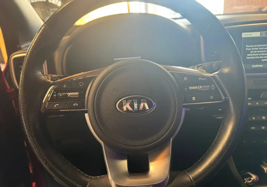 Gros plan sur le volant cuir noir du Kia Sportage rouge 2019, avec commandes intégrées et logo central visible.