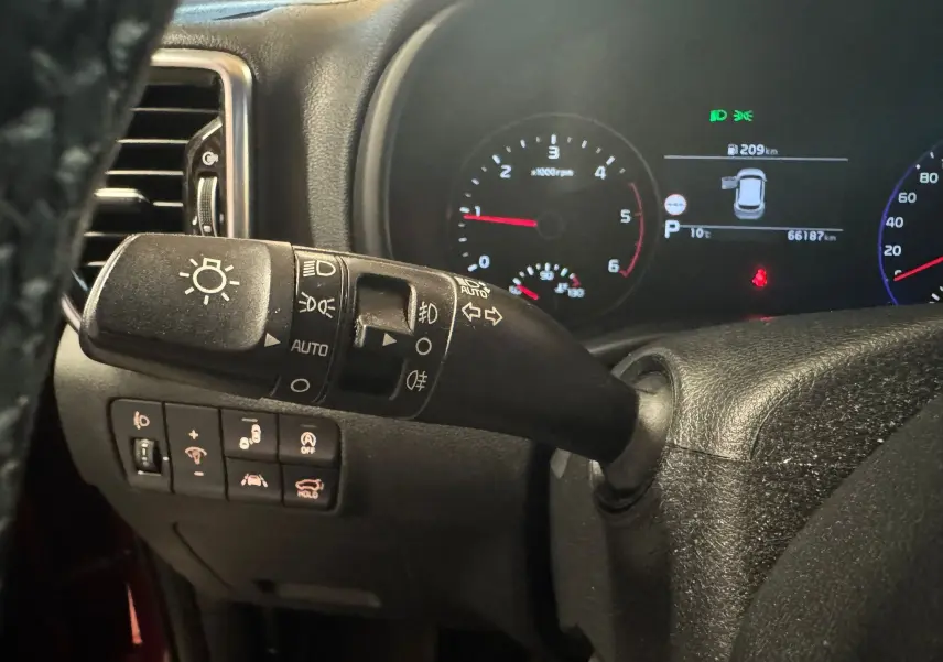 Gros plan sur la commande des phares et le tableau de bord numérique d'un KIA Sportage rouge, version 2019.