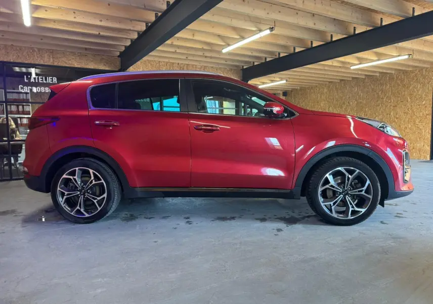 Vue de profil droit d'un KIA Sportage rouge 2019, version 1.6 CRDI GT Line, avec jantes alliage et toit noir.