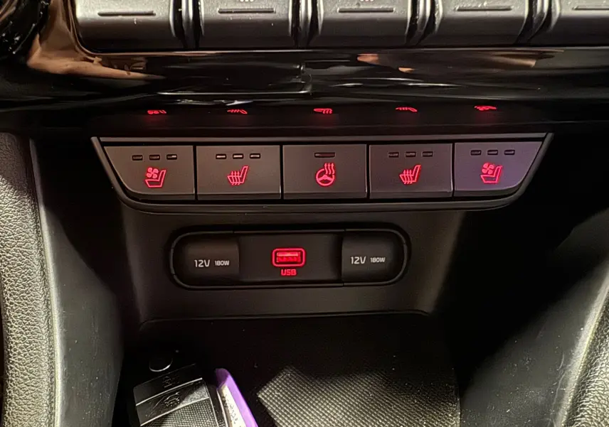 Gros plan sur les commandes rouges des sièges chauffants et ventilés ainsi que les prises USB et 12V du Kia Sportage rouge 2019.