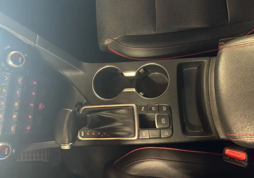 Vue plongeante sur la console centrale noire du Kia Sportage 2019, avec levier de vitesse automatique et coutures rouges.