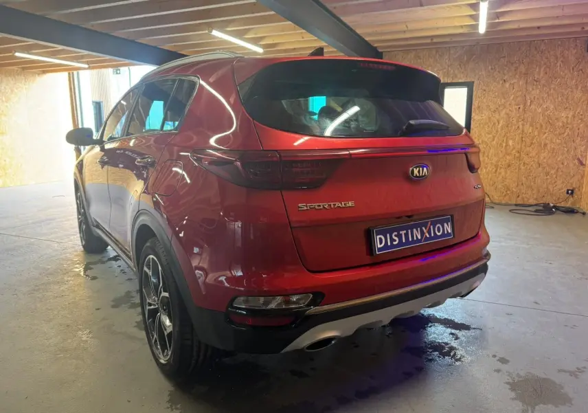 Vue 3/4 arrière droite d'un KIA Sportage rouge 2019 avec feux arrière sombres et double sortie d'échappement.