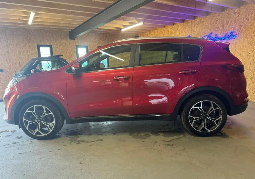 Vue de profil côté gauche d'un KIA Sportage rouge 2019, avec jantes alliage noires et détails sportifs visibles.