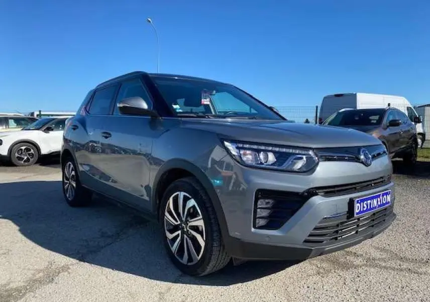 SsangYong Tivoli gris foncé en 3/4 avant droit, avec jantes alliage et feux LED distinctifs sous un ciel bleu.