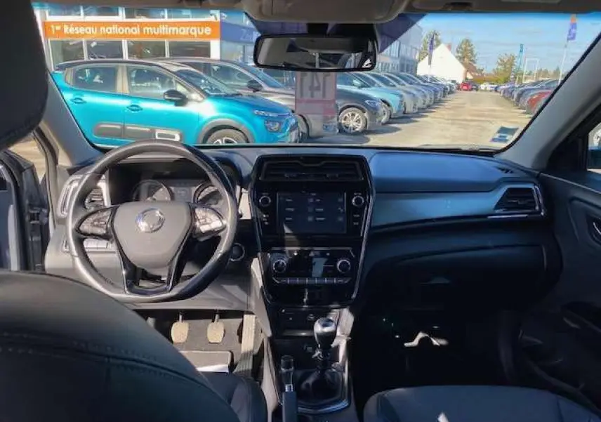 Vue intérieure avant du SsangYong Tivoli gris foncé montrant le tableau de bord et le volant cuir avec écran tactile central.