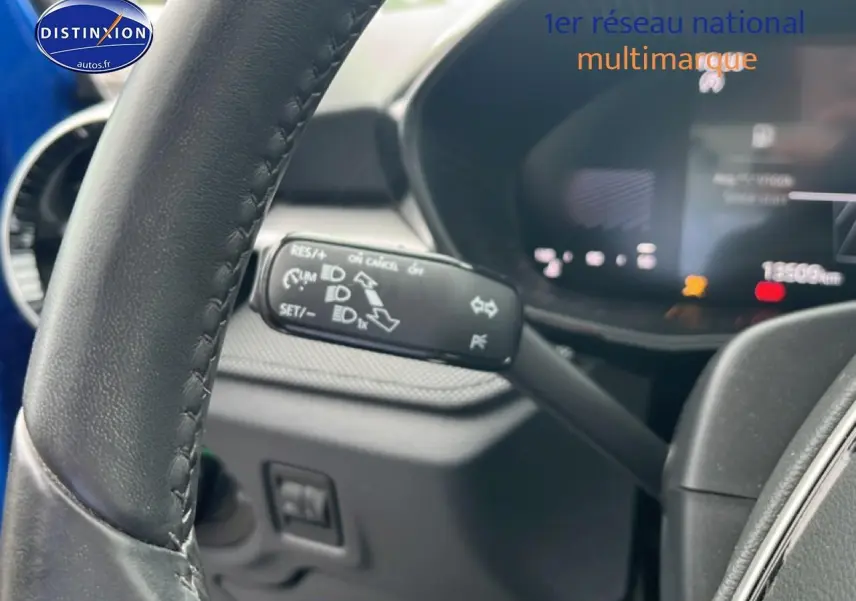 Gros plan sur le volant cuir et la commande multifonction noire dans l'habitacle sombre d'une Skoda Fabia bleue.