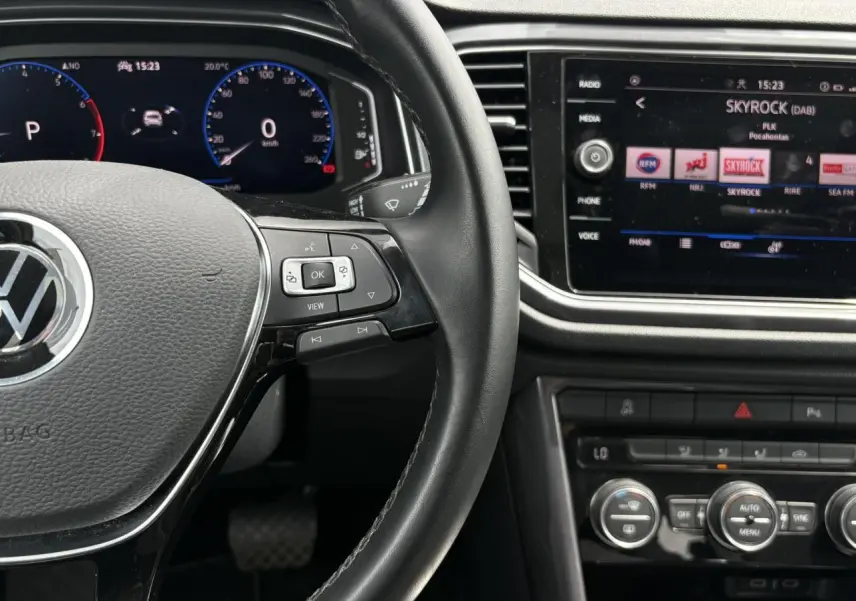 Vue rapprochée de l’intérieur du Volkswagen T-Roc 1.5 TSI 2021, volant cuir noir et écran tactile central allumé.