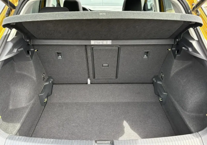 Vue intérieure du coffre ouvert du Volkswagen T-Roc jaune curcuma, montrant le plancher et la cloison arrière en tissu gris.