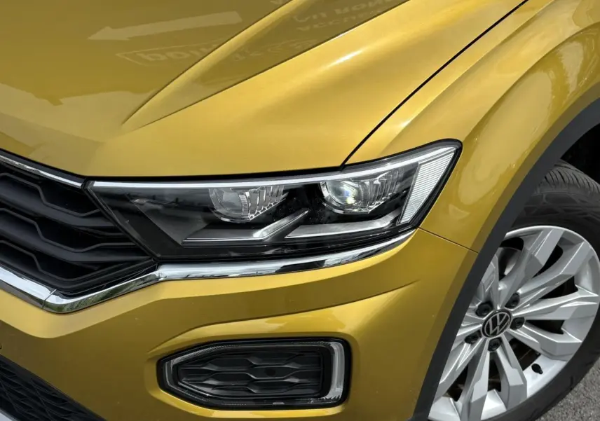 Gros plan sur l'avant droit du Volkswagen T-Roc jaune curcuma, mettant en valeur le phare LED et la jante alliage 17 pouces.