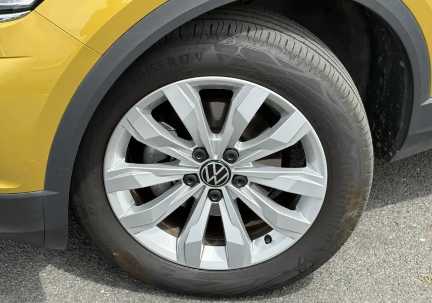 Gros plan sur la roue avant gauche d’un Volkswagen T-Roc jaune curcuma avec jante alliage 17 pouces et logo VW central.