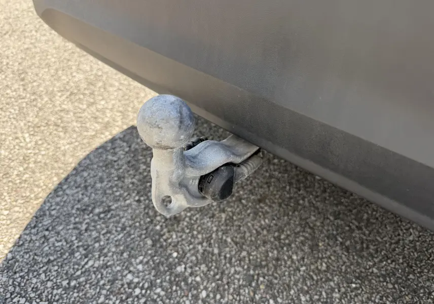 Gros plan sur le crochet d'attelage escamotable gris sous le pare-chocs arrière d'un Volkswagen Tiguan bleu.