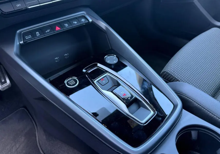 Vue rapprochée de la console centrale noire brillante avec levier de vitesses automatique et bouton start/stop d’une Audi A3 Sportback.