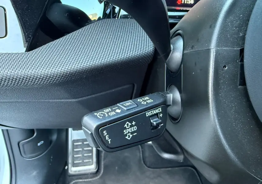 Gros plan sur la commande de régulateur de vitesse au volant d’un Audi A3 Sportback blanc Glacier métallisé.