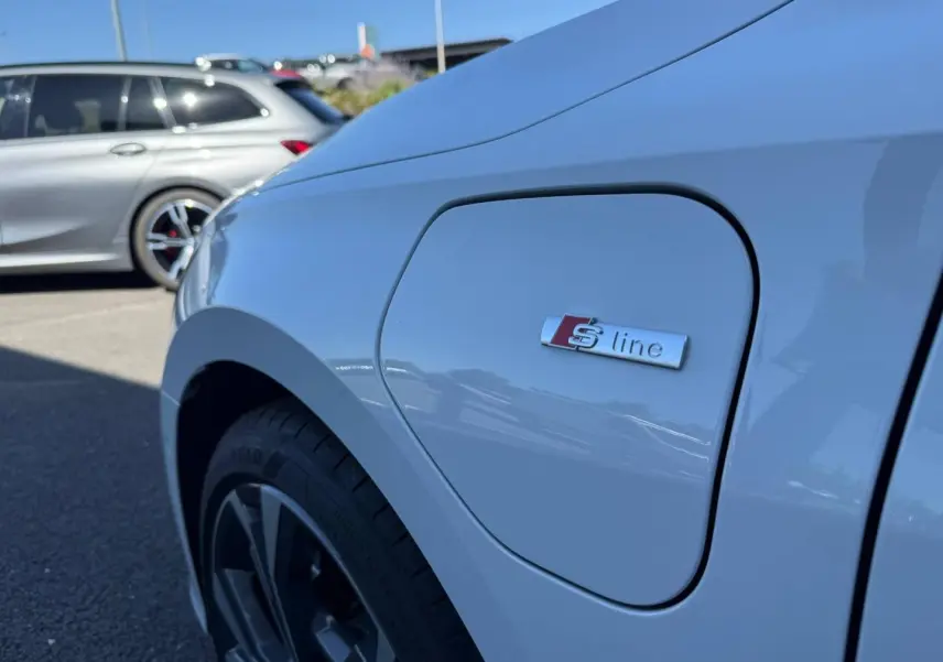 Gros plan sur la trappe de recharge côté avant gauche d’une Audi A3 Sportback blanc Glacier métallisé avec logo S line.