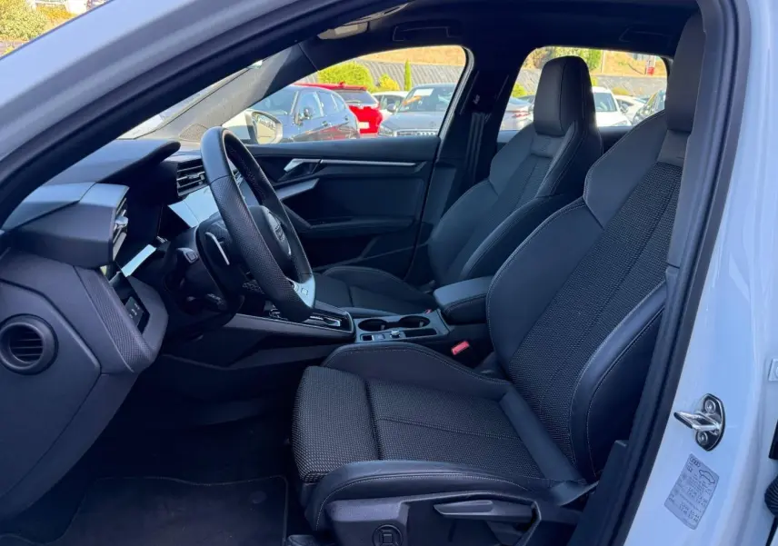 Vue intérieure côté conducteur de l'Audi A3 Sportback 2025, sièges sport noirs et volant cuir multifonction.