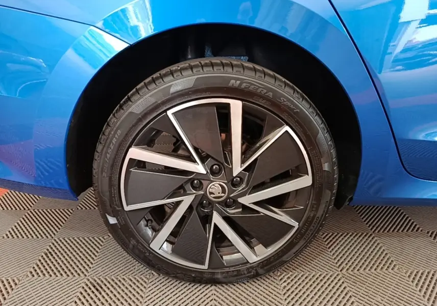 Gros plan sur la roue arrière droite d’une Skoda Octavia bleu avec jante alliage noire et argentée.