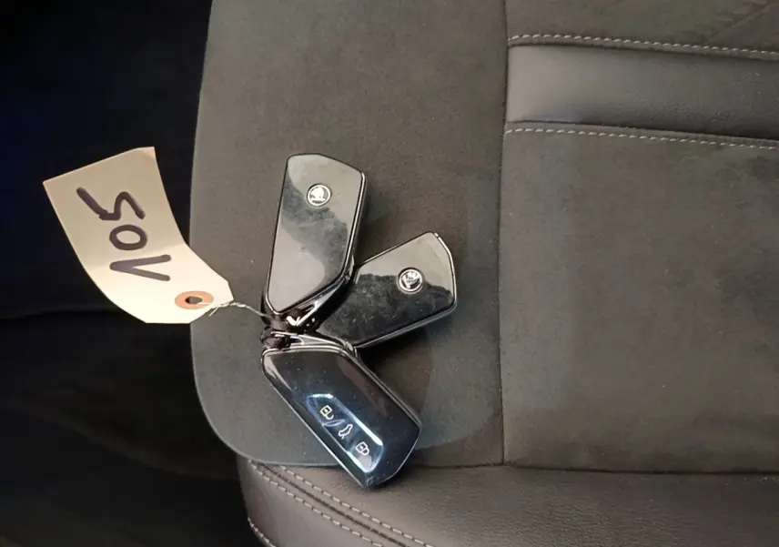 Gros plan sur trois clés noires SKODA posées sur un siège en tissu gris foncé, sans vue du véhicule.