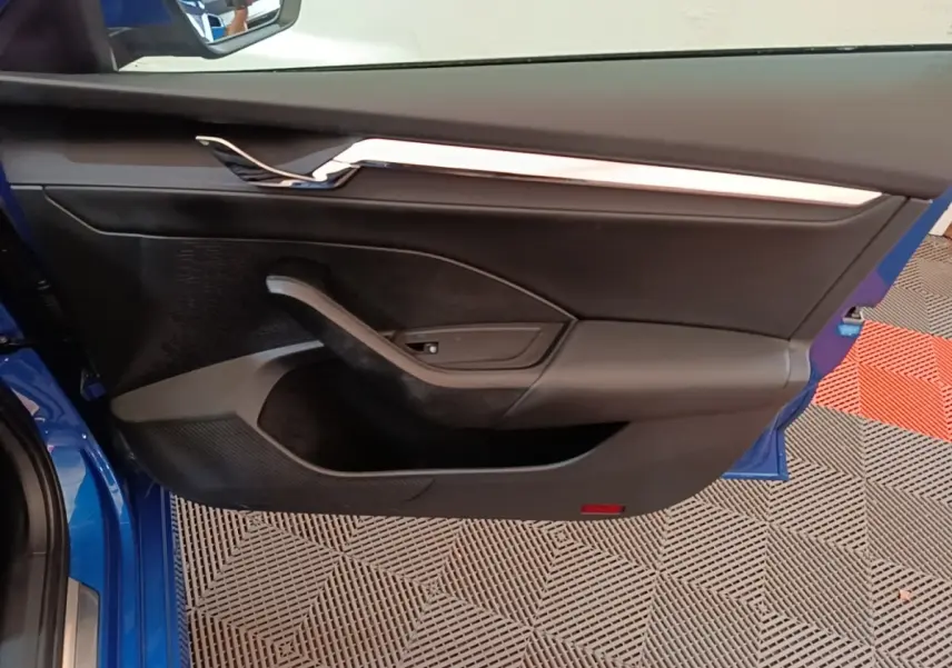 Vue intérieure de la porte avant gauche d’une Skoda Octavia bleu 2022 avec garniture noire et insert chromé.