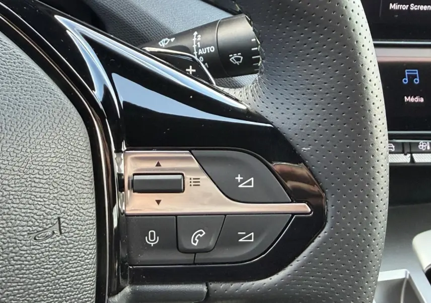 Gros plan sur les commandes multifonctions noires et chrome du volant cuir perforé côté gauche du Peugeot 408 Hybrid 2025.