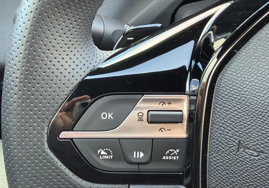 Gros plan sur les commandes de régulateur de vitesse au volant perforé noir de la Peugeot 408 Hybrid 2025.