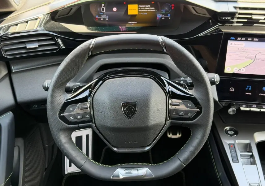 Vue intérieure centrée sur le volant cuir noir GT avec coutures vertes et tableau de bord numérique du Peugeot 408 Hybrid 2025.