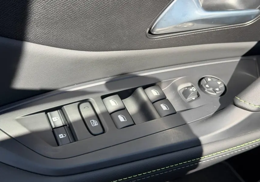 Commande des vitres et rétroviseurs sur la porte côté gauche d’une Peugeot 408 Hybrid 2025 avec surpiqûres vertes.