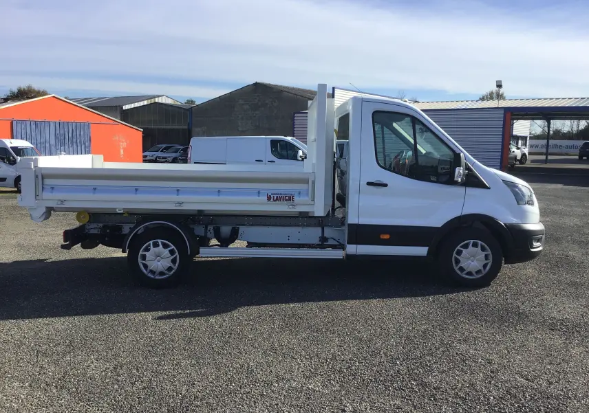 Profil côté gauche d'un Ford Transit Chassis Cabine blanc avec benne basculante et bras polybenne sur un parking extérieur.