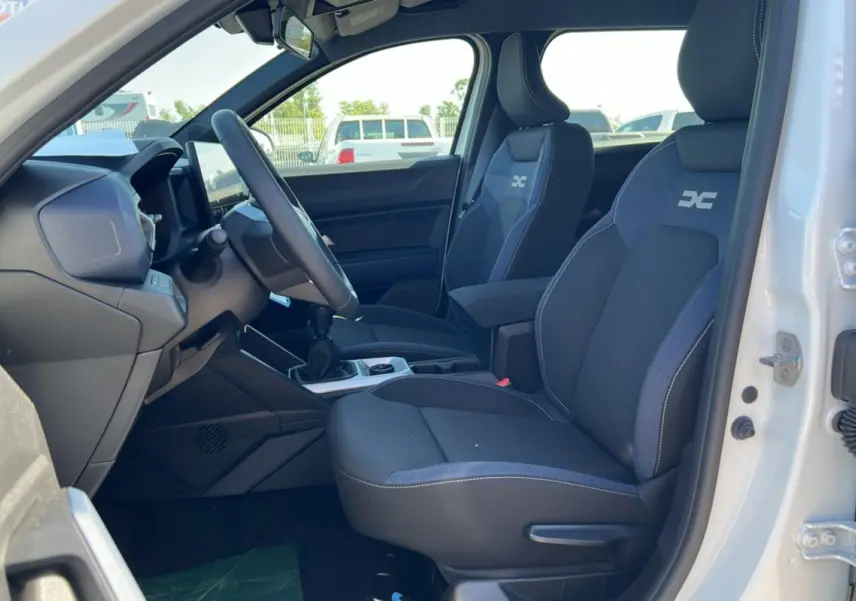 Intérieur du Dacia Bigster blanc glacier vu côté conducteur, sièges noirs avec logo DC et boîte manuelle visible.