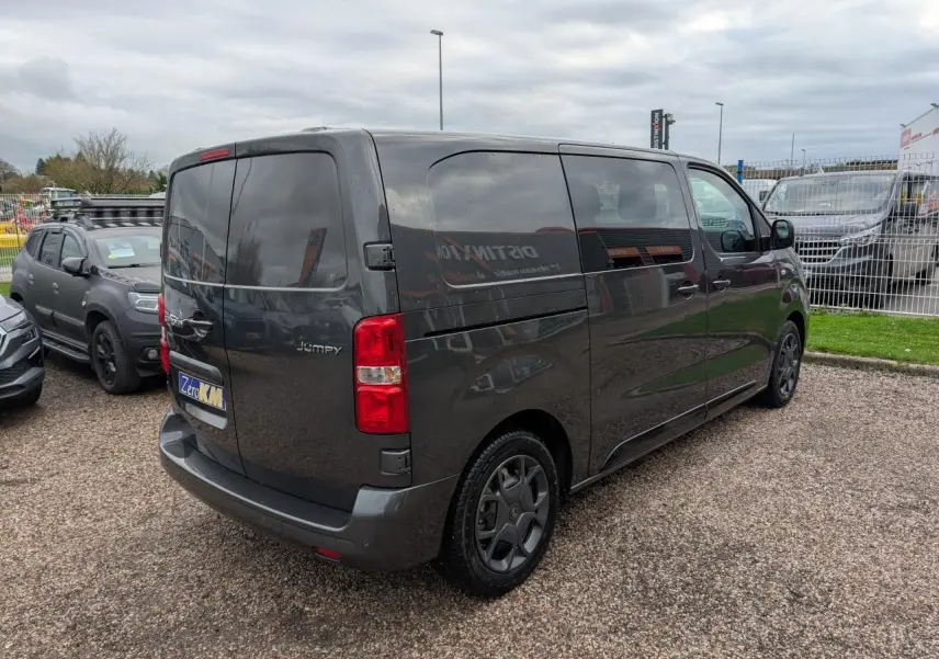 Vue 3/4 arrière droite d'un Citroën Jumpy gris foncé avec portes arrière battantes et vitres teintées.