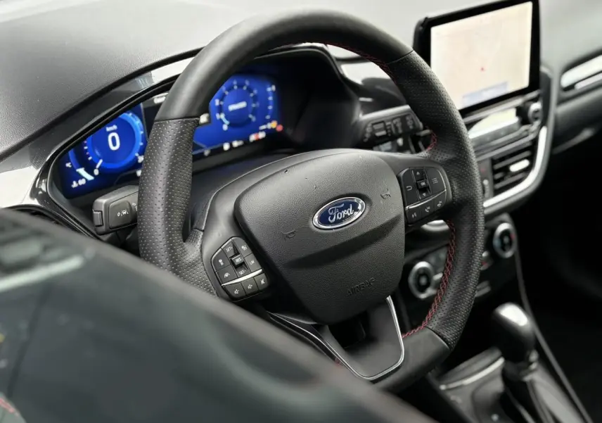 Vue rapprochée du volant ST-Line noir avec surpiqûres rouges et tableau de bord numérique bleu du Ford Puma 2023.