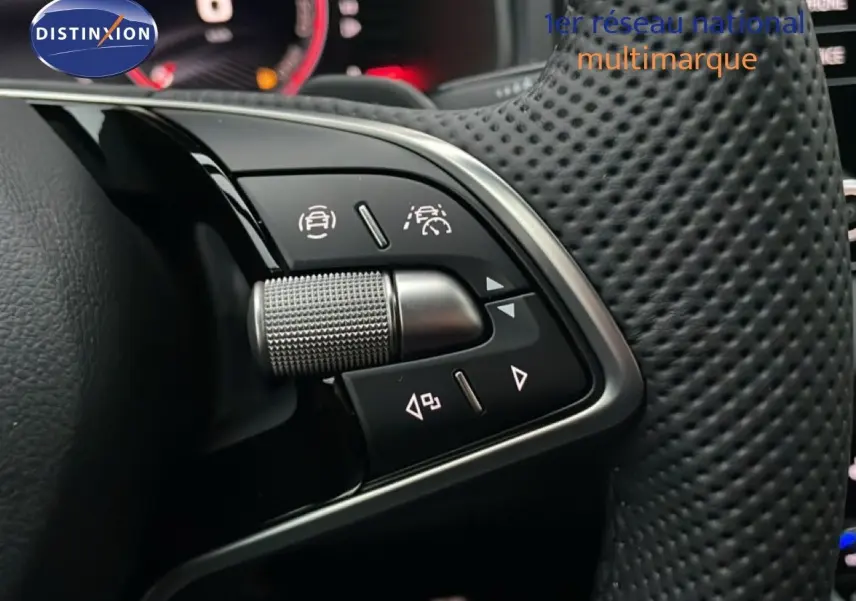 Gros plan sur les commandes au volant perforé du Skoda Karoq gris argent 2025, avec tableau de bord numérique en arrière-plan.