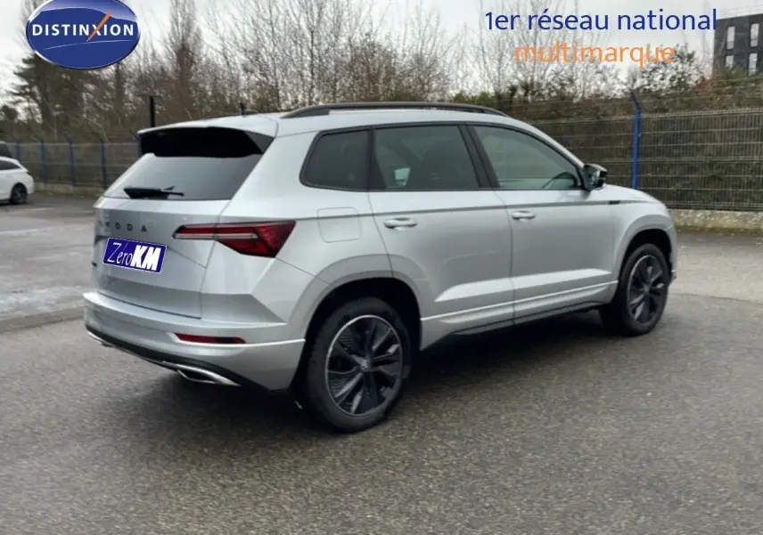 Vue 3/4 arrière droite d’un Skoda Karoq gris argent métal 2025 avec jantes noires et toit ouvrant.