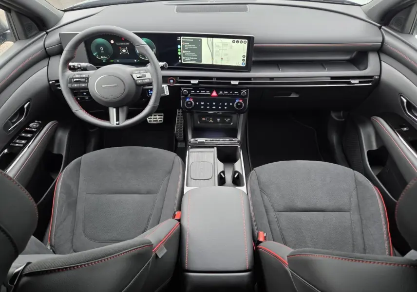 Vue intérieure frontale du Hyundai Tucson N Line 2025, avec sellerie cuir/alcantara noire et surpiqûres rouges, tableau de bord numérique et écran tactile large.