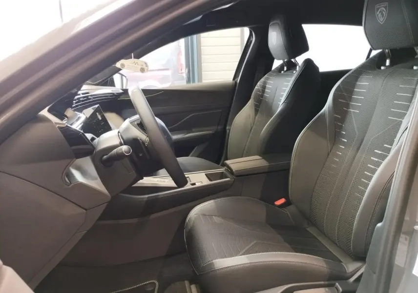 Intérieur avant droit de la Peugeot 308 gris selenium, sièges noirs avec surpiqûres vert Adamite et logo Peugeot brodé.