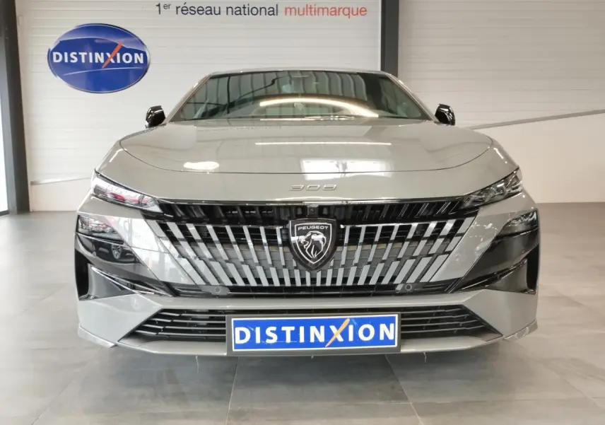 Vue frontale d'une Peugeot 308 gris selenium avec calandre noire et blason Peugeot lumineux, en intérieur showroom.