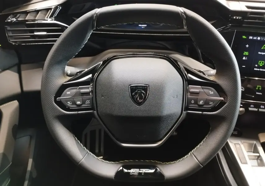 Volant compact GT en cuir noir avec surpiqûres vert Adamite et logo Peugeot au centre, vue de face.