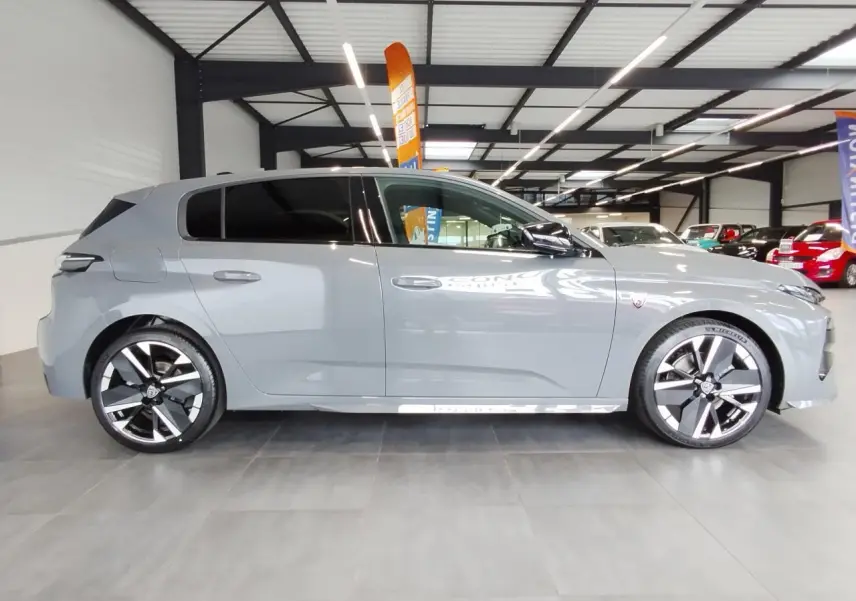 Vue de profil droit d'une Peugeot 308 gris selenium avec jantes alliage bi-tons et vitres surteintées dans un showroom.