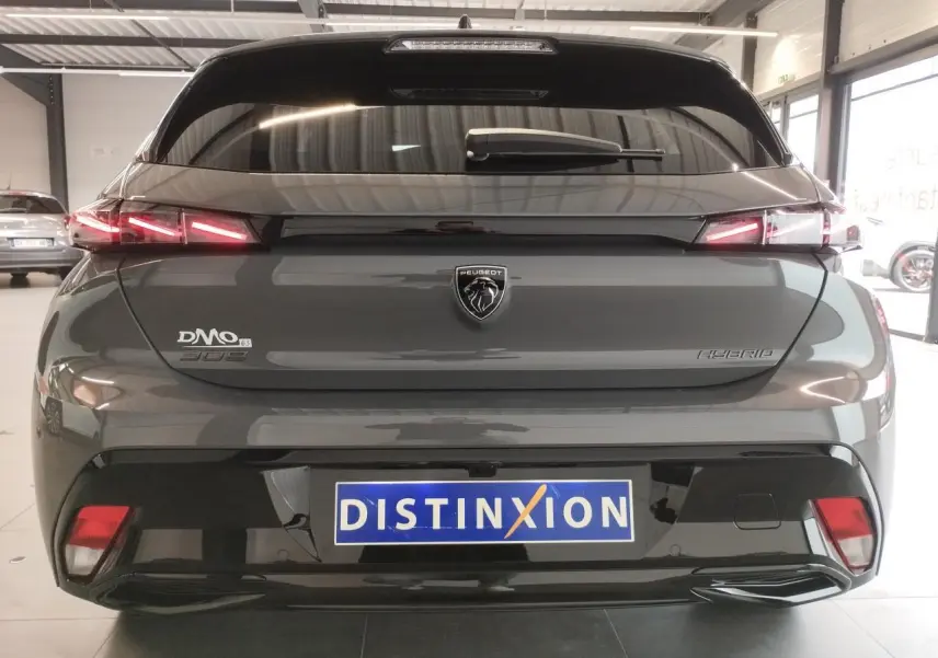 Vue arrière d'une Peugeot 308 hybride gris selenium avec feux arrière LED en forme de griffes et logo Peugeot central.