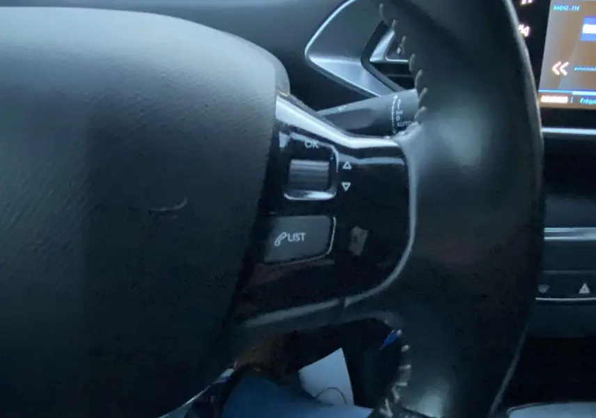 Gros plan sur le volant noir de la Peugeot 308 2020, avec commandes intégrées et écran tactile partiellement visible.