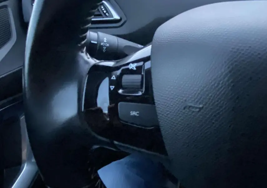 Gros plan sur le volant noir de la Peugeot 308 gris clair, avec commandes audio intégrées sur la branche gauche.