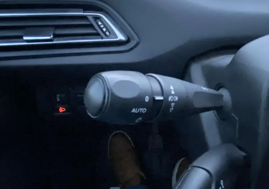 Détail du commodo d'éclairage avec réglage automatique dans l'habitacle d'une Peugeot 308 gris clair.
