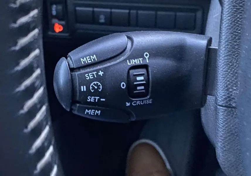 Commande de régulateur de vitesse au volant d'une Peugeot 308 gris clair, vue rapprochée côté gauche.